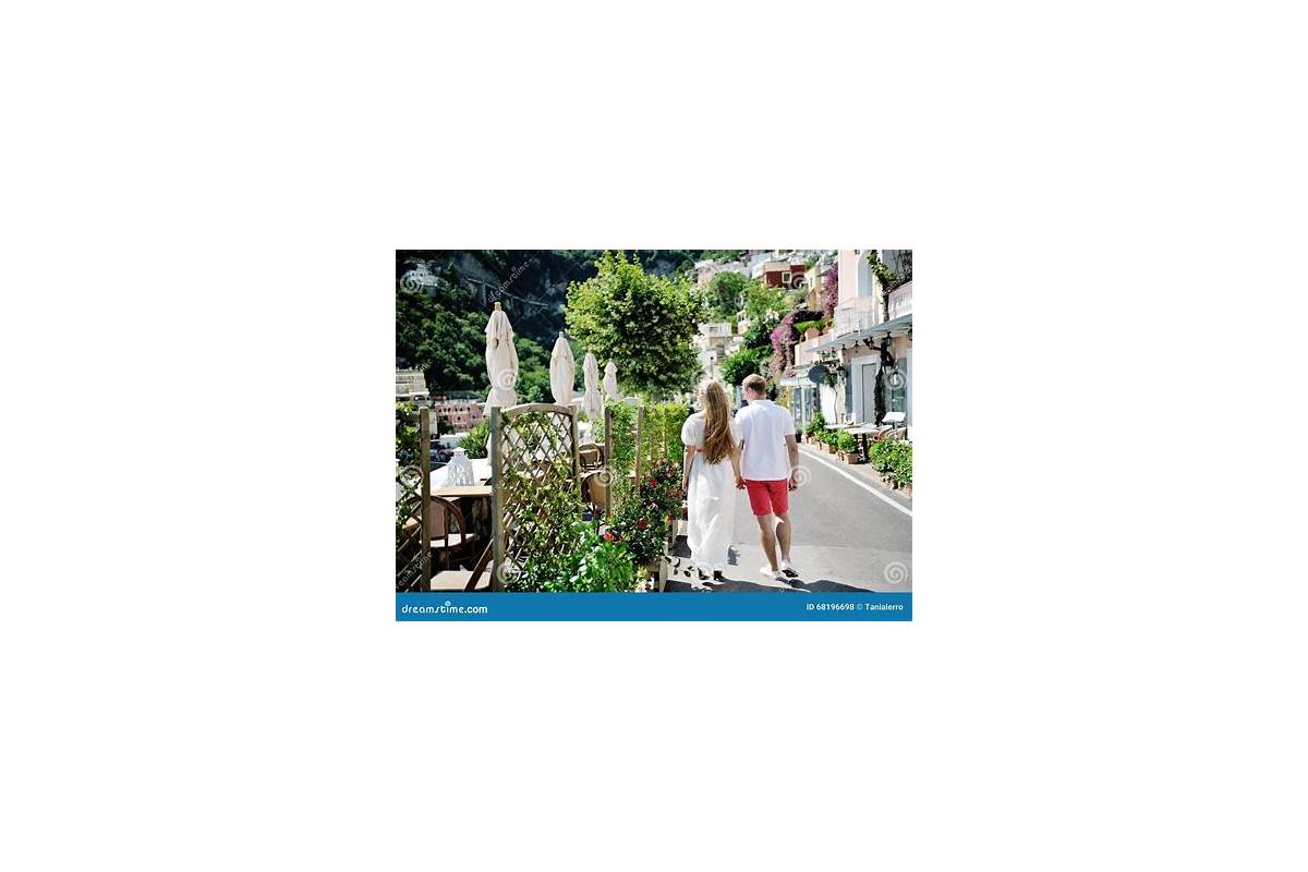 Couple walking hand in hand through the streets of Positano, Amalfi Coast, with colorful buildings and the sea in the background.